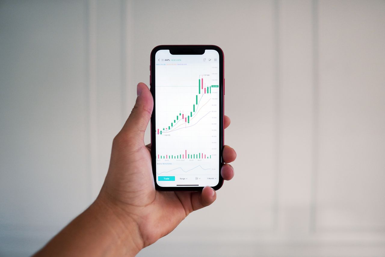 Gros plan sur une main tenant un smartphone affichant un graphique boursier à l’intérieur.